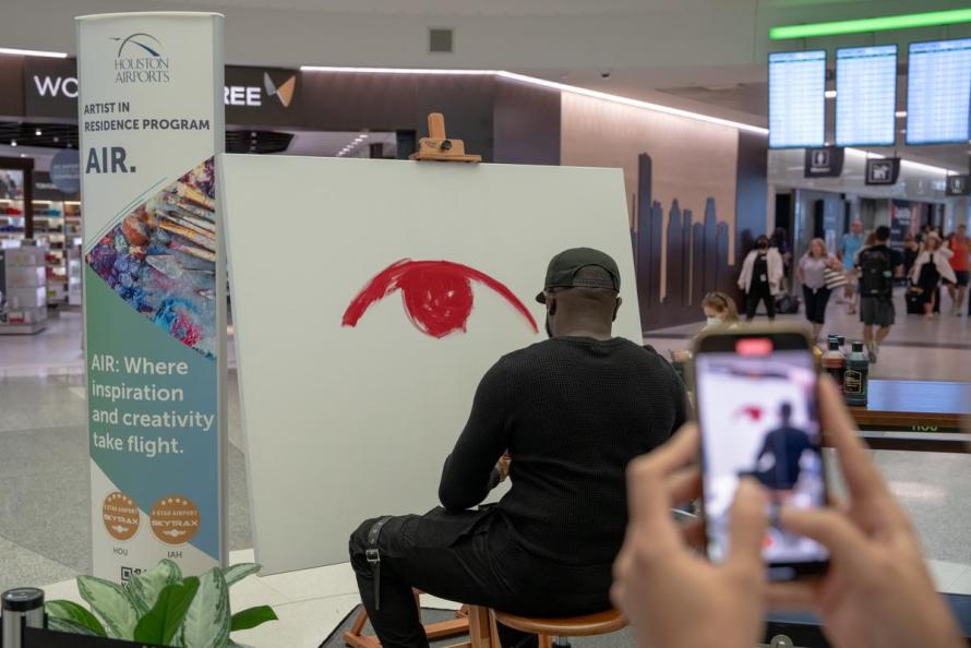 Travelers watch as Mathieu Jean Baptiste paints art inside Hobby Airport 