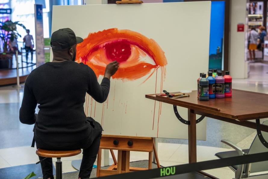 Travelers watch as Mathieu Jean Baptiste paints art inside Hobby Airport 